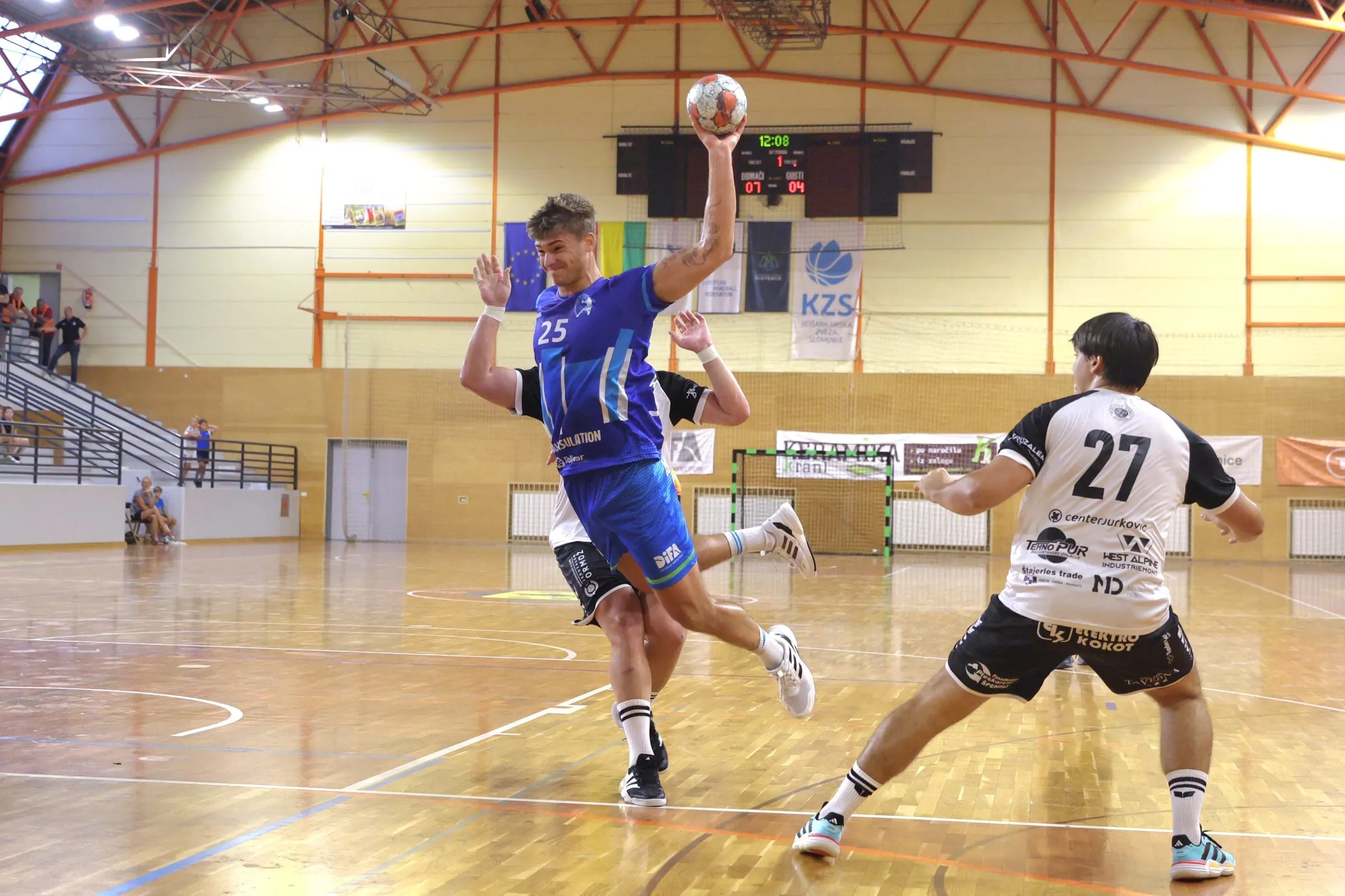 Igralec RD Škofja Loka s številko 25 v modrem dresu strelja proti RK Jeruzalem Ormož ob vodstvu 7:4
