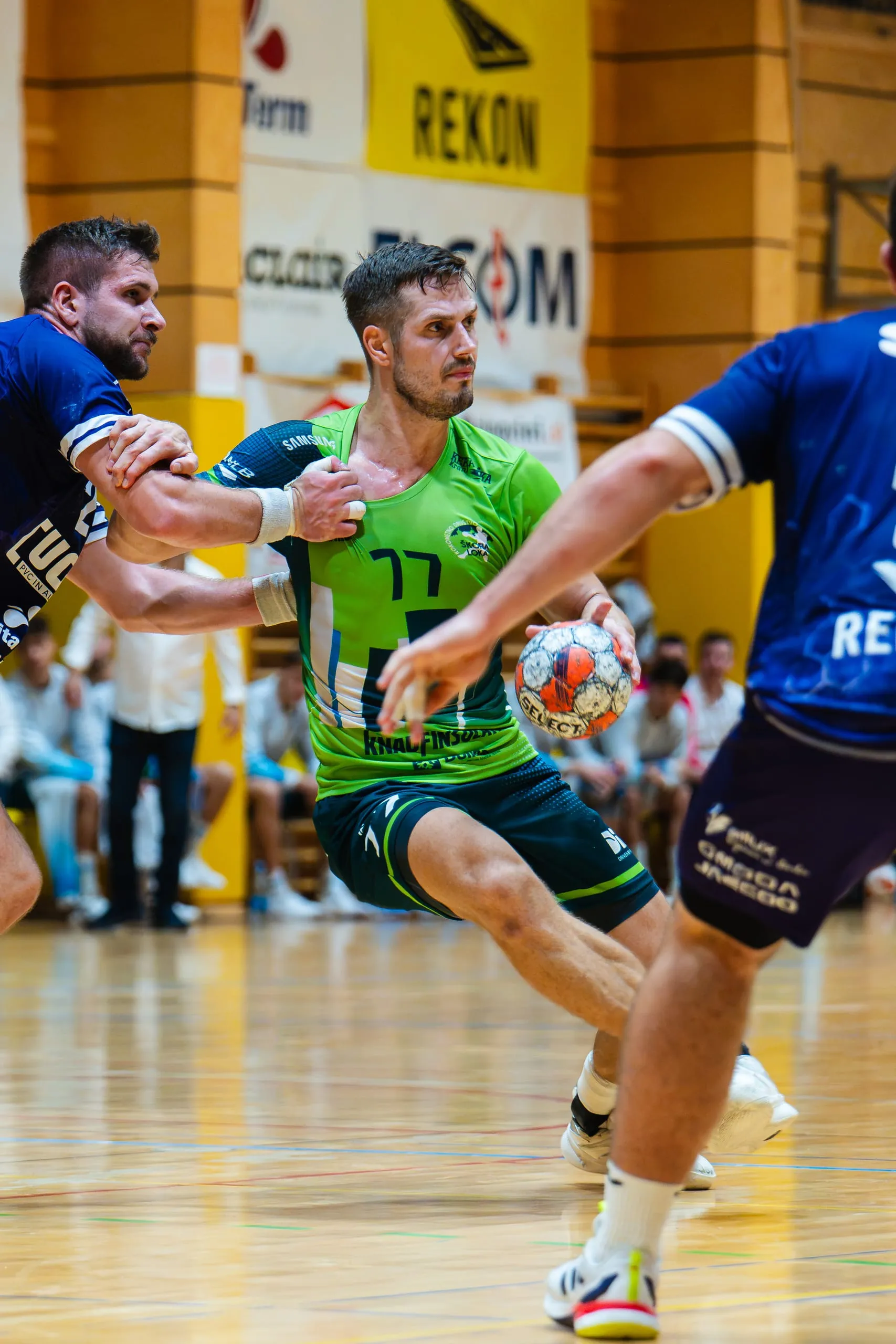 Igralec RD Škofja Loka s številko 77 v zelenem dresu prodira z žogo, branilec RK Sviš ga drži za roko